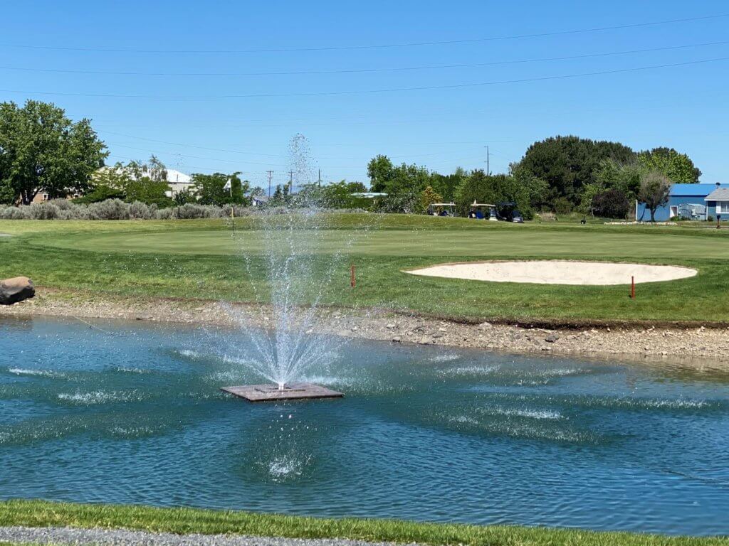 Water fountain spraying from pond surrounded by green grass.